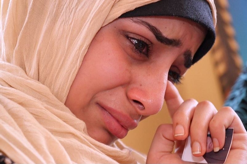 A young woman wipes away a tear while holding a photo of her mother.