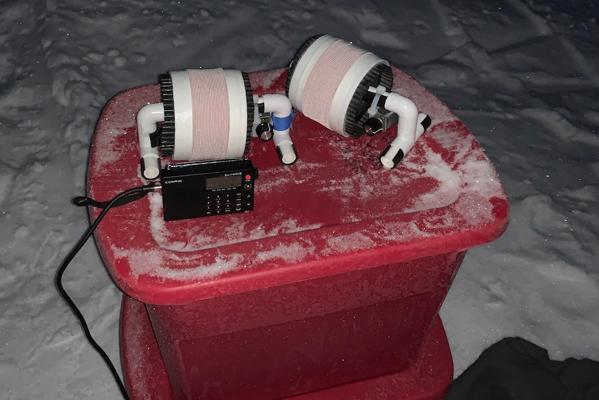 Radio antennae on top of a red plastic container in the snow.