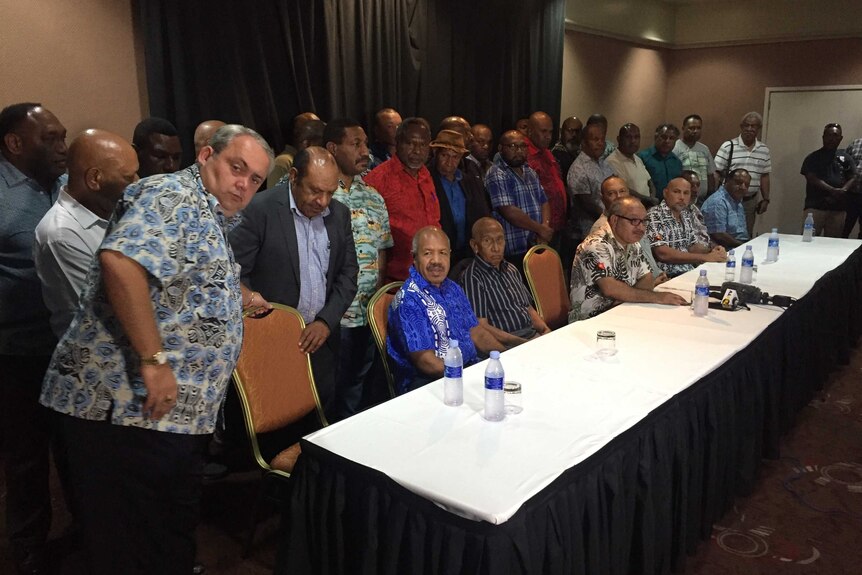 A large group of MPs stand behind a table where PNG Prime Minister Peter O'Neill.
