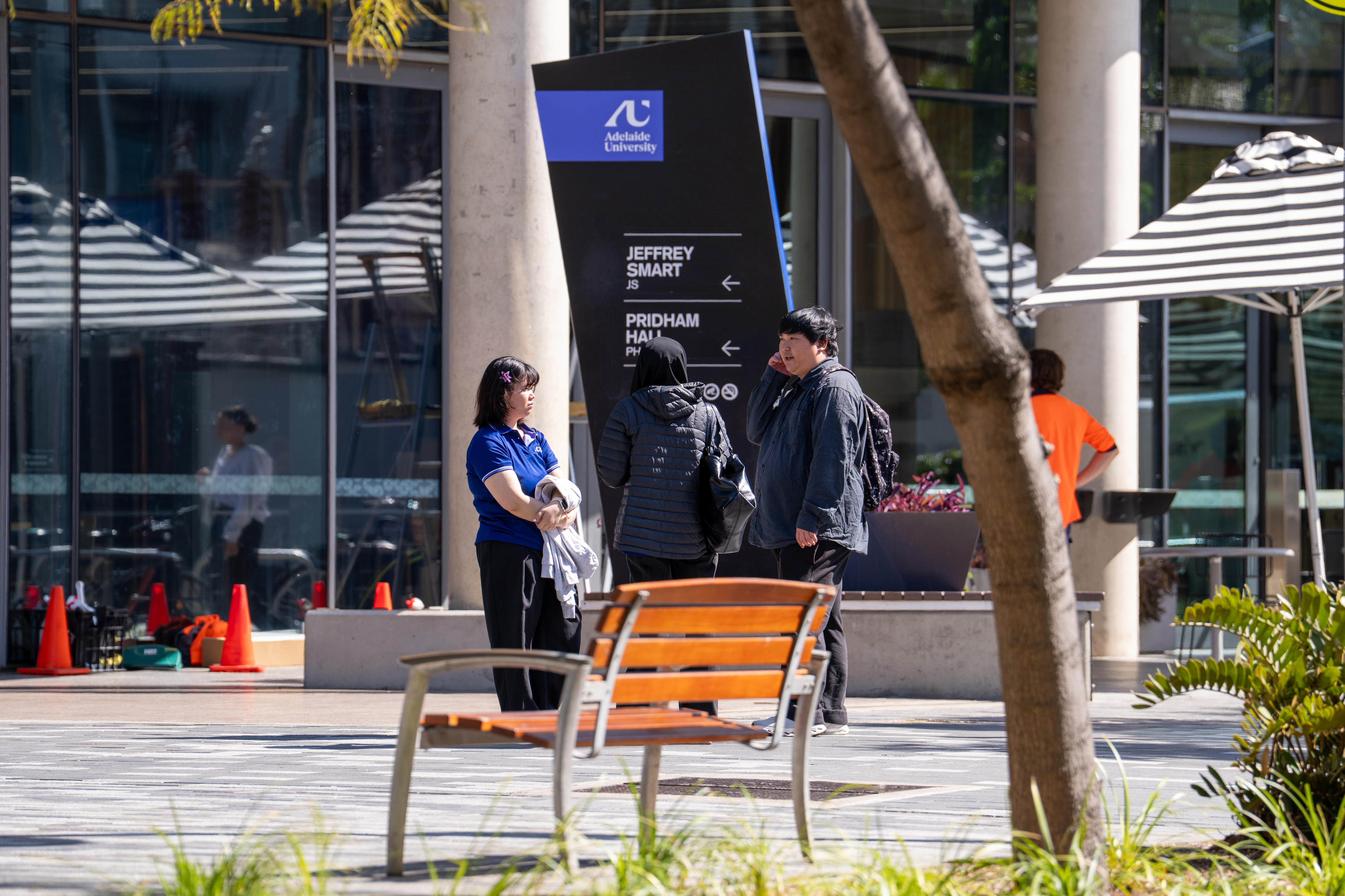three students talk in front of the new Adelaide University sign