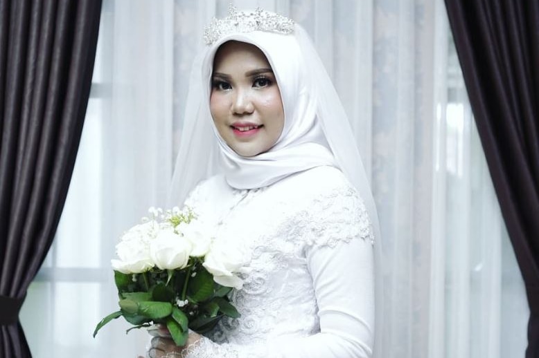 A woman poses in a white wedding dress with a bunch of white flowers