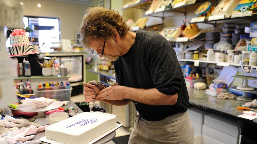 A man in a cake shop ices a cake with the words Happy Birthday on it.