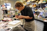 A man in a cake shop ices a cake with the words Happy Birthday on it.