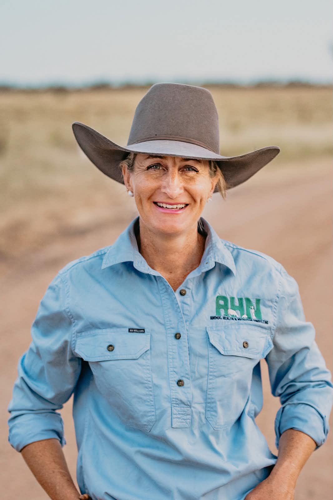 A woman in a brown felt hat smiles to camera