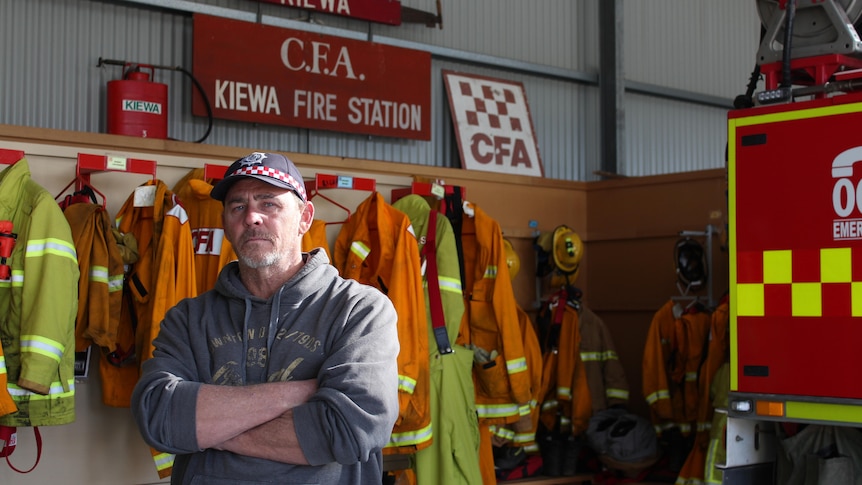 A man stands with his arms folded next to a fire truck with CFA clothes on the wall behind him.