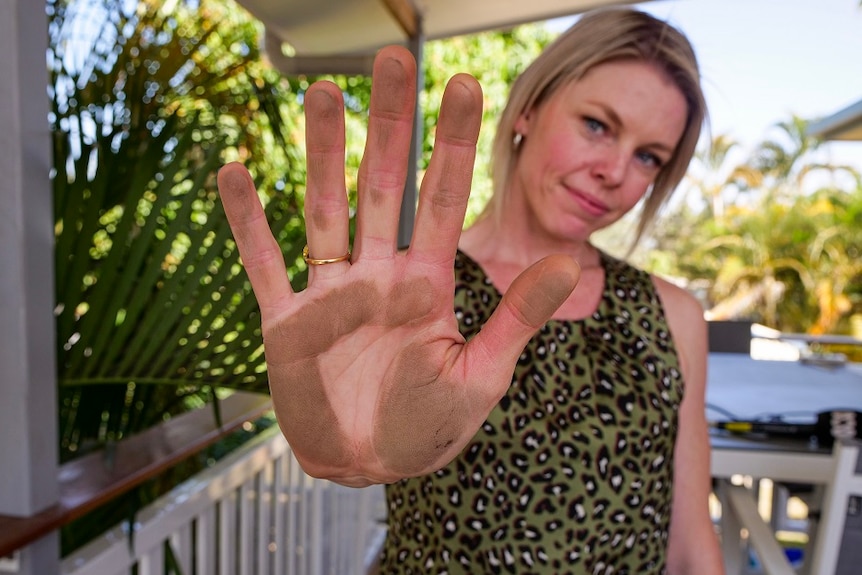 Moranbah resident shows her palm covered in dust after wiping it along a railing.