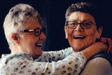 Two older women with big smiles, hugging.