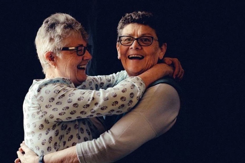 two older women with grey hair and glasses hugging