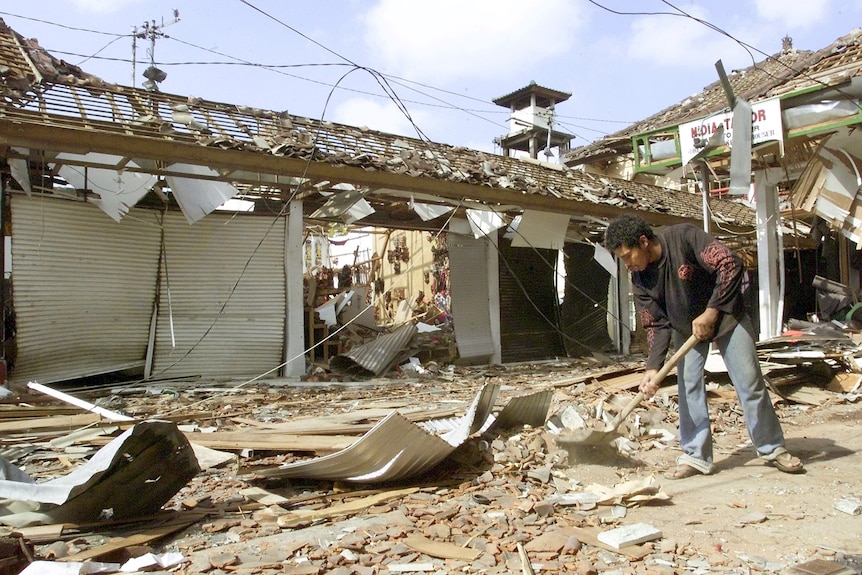 A Balinese man clears debris surrounded by blown out buildings.