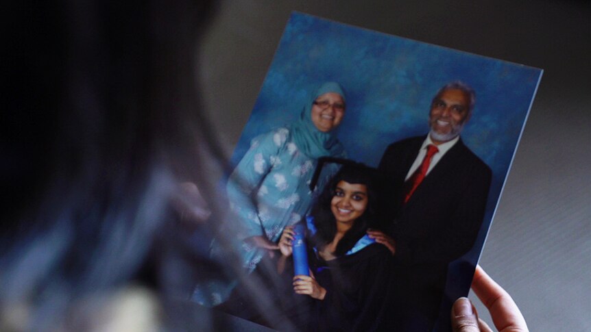 Photograph of Zoya Patel graduating with her parents standing behind her.