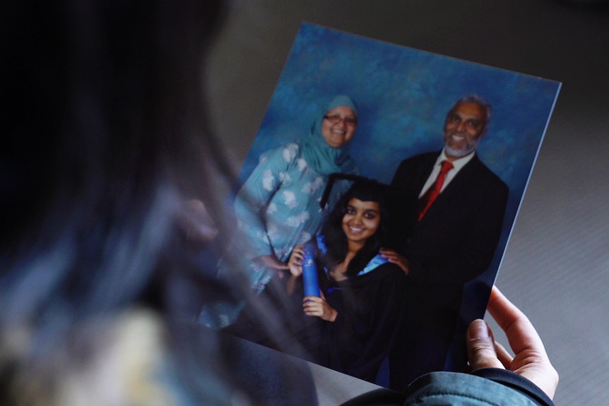 Photograph of Zoya Patel graduating with her parents standing behind her.