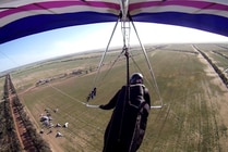 A hang glider in the sky over open fields.