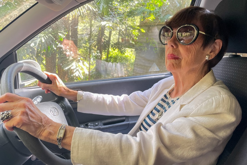 A woman wearing sunglasses in the drivers seat with hands on the wheel.  