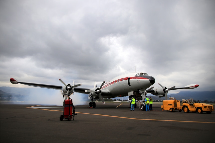 A large aeroplane with two propellers stands on the tarmac under a foreboding grey sky.