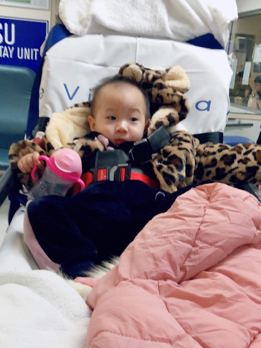A baby girl wearing a fluffy leopard print coat strapped onto a stretcher.