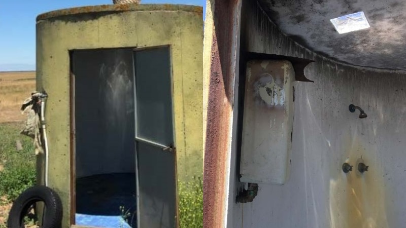 An image of an old water tank with its door open and a shower head and taps on the inside of the tank