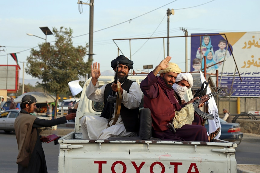 Three men with guns wave from the tray of a ute in Kabul.
