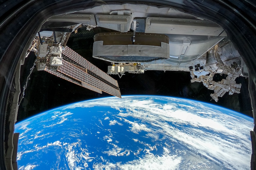 Une image de l'ISS qui montre la terre de loin au-dessus, avec sur la moitié supérieure la station spatiale elle-même