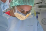 An Aboriginal woman in surgical scrubs with a green cap and a yellow mask.