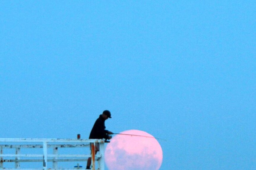 The full moon rises behind a man fishing off the Point Lonsdale pier