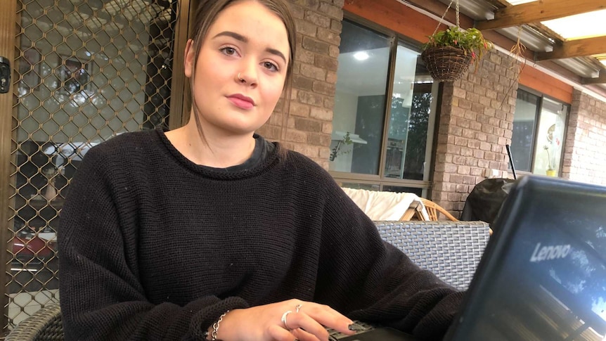 Gabrielle Kidd sits at an outdoor table and uses a laptop