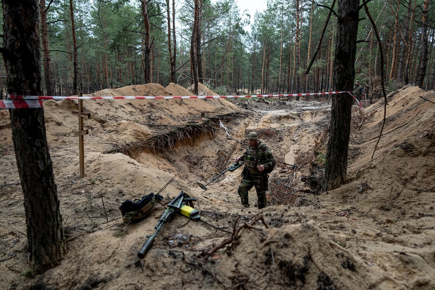 A Ukrainian serviceman uses a metal detector to inspect a mass grave in the recently retaken area of Izium.