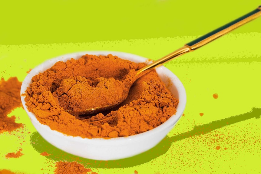 A small bowl of turmeric with a spoon in it