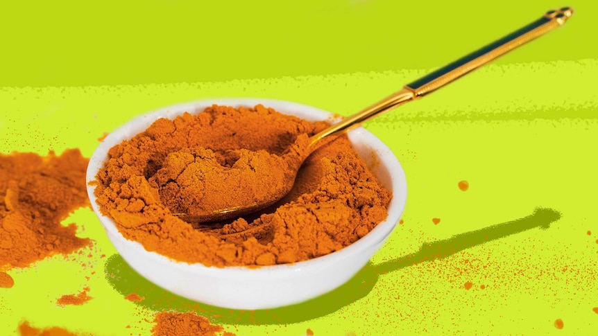 A small bowl of turmeric with a spoon in it