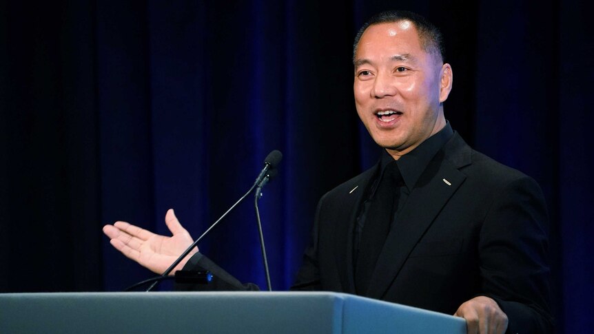 Guo Wengui stands at a podium in a black suit