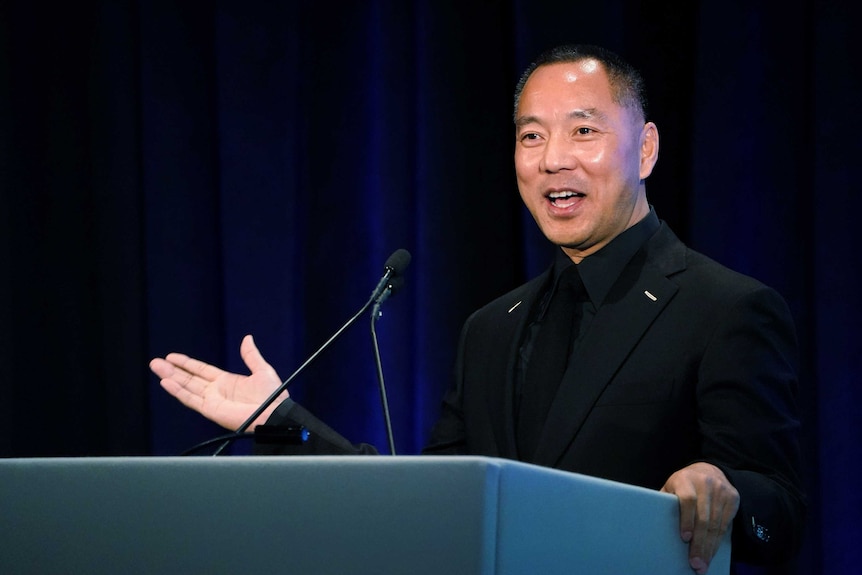 Guo Wengui stands at a podium in a black suit