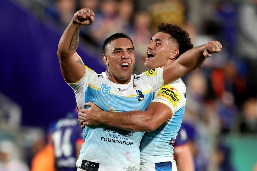 Two Gold Coast Titans players celebrate. One raising his arms celebrating while being hugged by his teammate