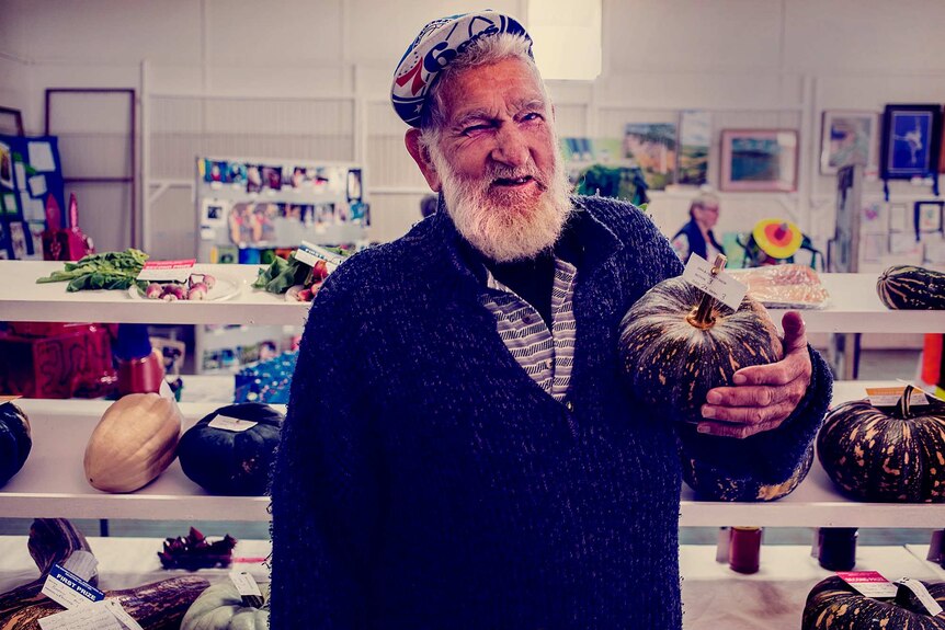 Older man holds a pumpkin.