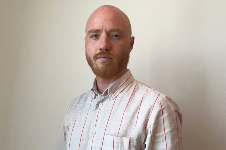 A man standing in front of a white wall. 