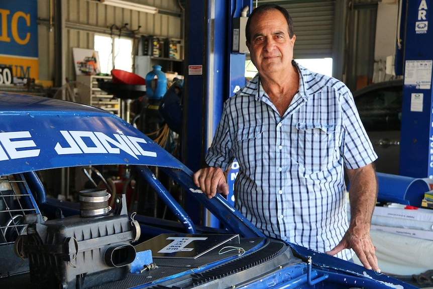 Flood victim Lubo Jonic stands beside his son’s race car in his warehouse at Goodna.