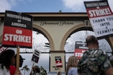 Picketers hold signs saying writers guild of america on strike in front of paramount pictures gate 