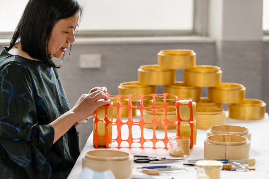 Jenny Zhe Chang looks down as she handles a latticed orange piece of art.