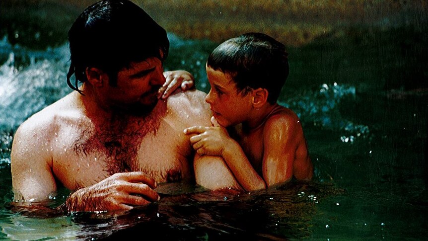 A young boy in a pool with his dad.