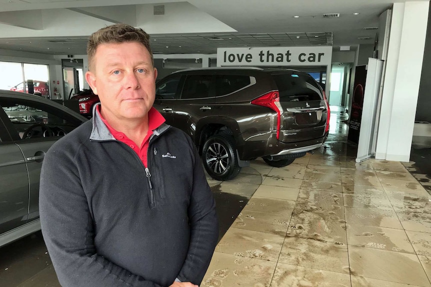James Johns stands in front of cars in his water-damaged car dealership.