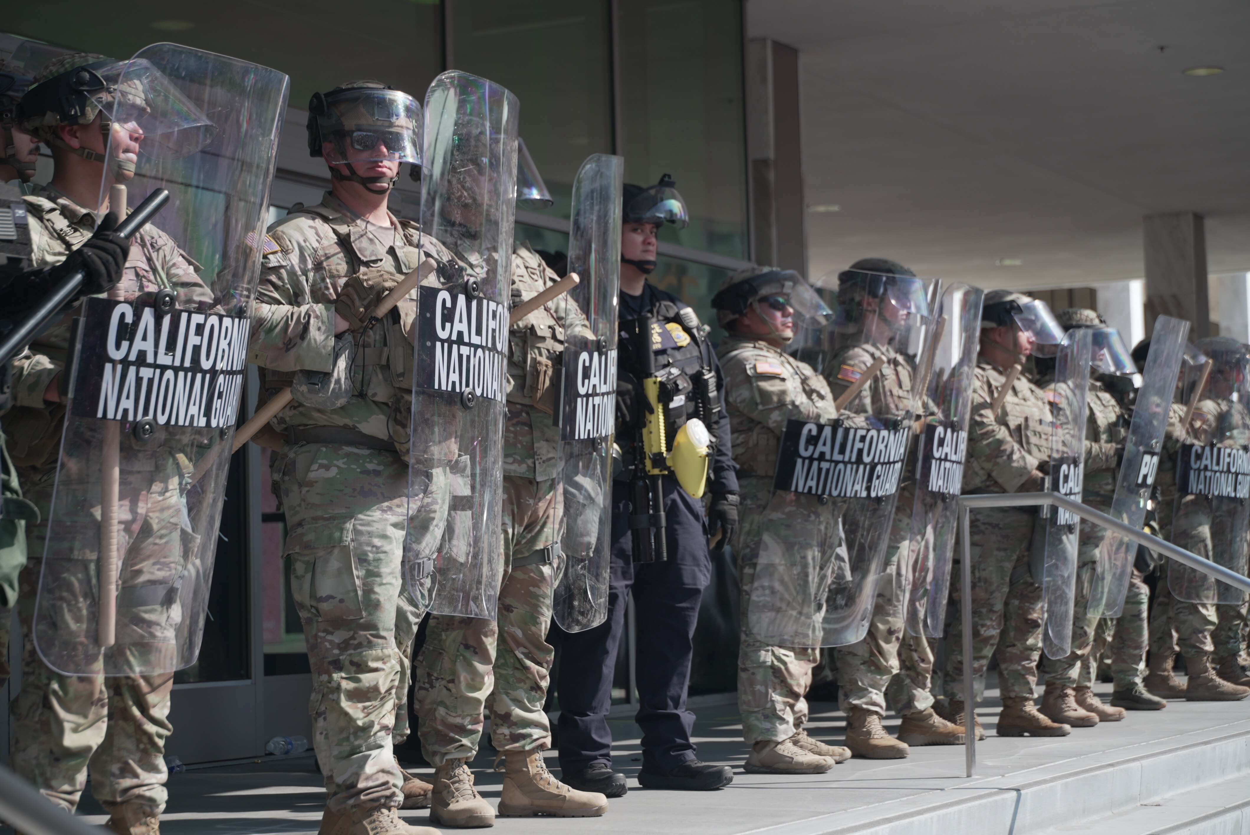 A row of National Guard officers in uniform holding up riot shields.