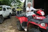 A woman sits on a quad bike outside a shed while men gather behind her.