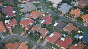 Houses predominantly with red roofs are seen form above, with two suburban streets in view.