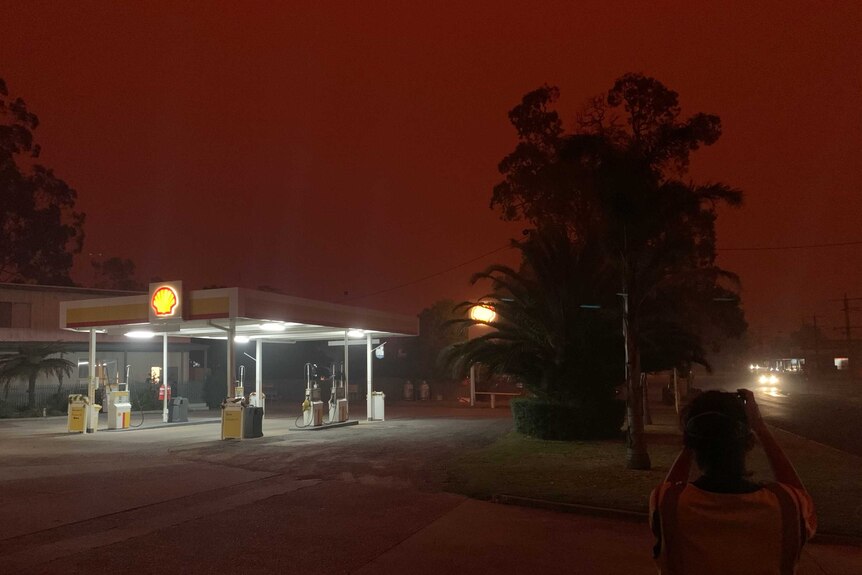 A service station lights up under a red sky.