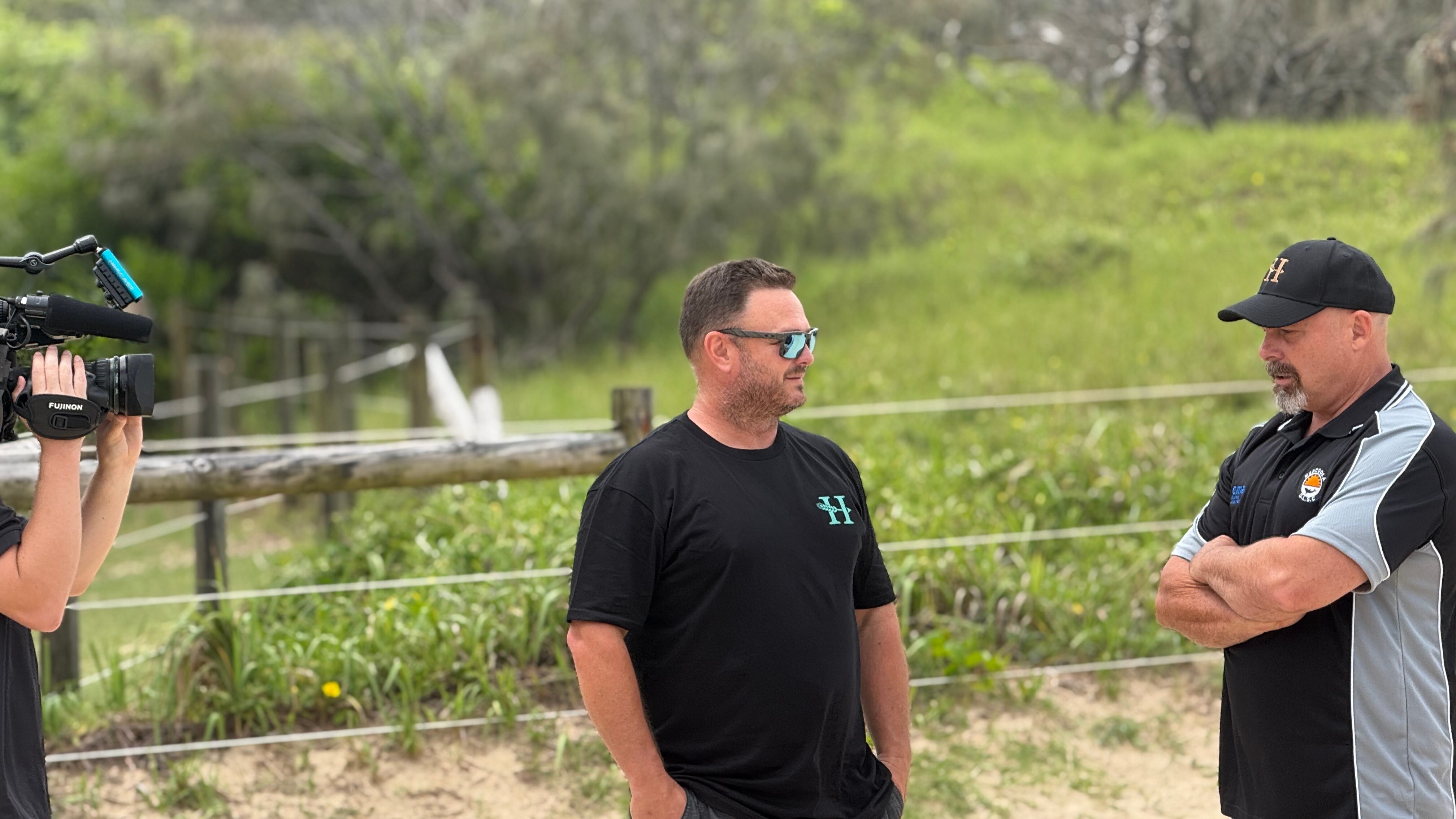 Matt Neale stands on the beach wearing a black tshirt and sunglasses