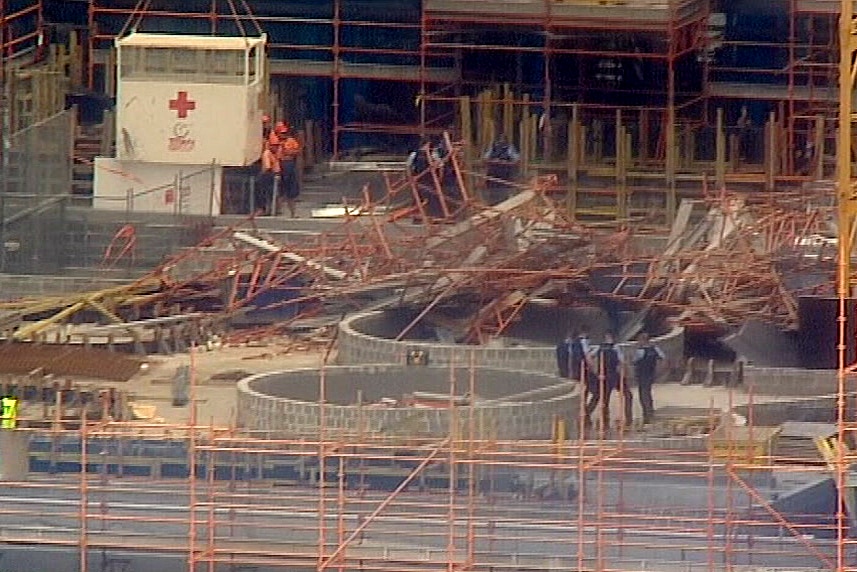 Police and workers in hard hats stand near a pile of red metal at a work site.