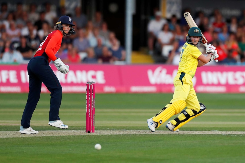 A cricketer strokes the ball square of the wicket as the wicketkeeper watches the ball race away.