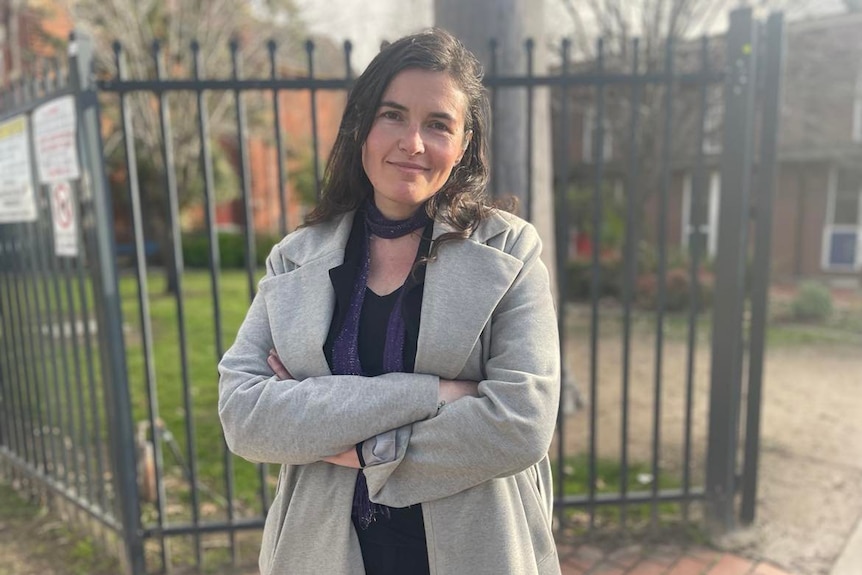 woman with dark hair grey coat standing with arms crossed