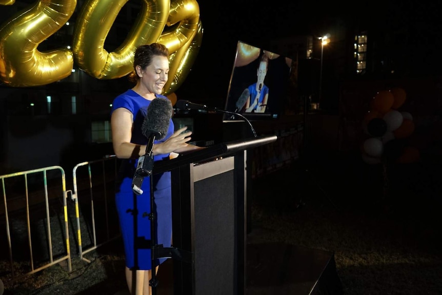 An wide image of Lia Finocchiaro speaking at a lecturn in the evening to supporters