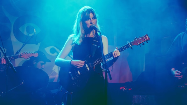 A woman, Juice Webster, on stage playing guitar and singing. She wears a black dress.