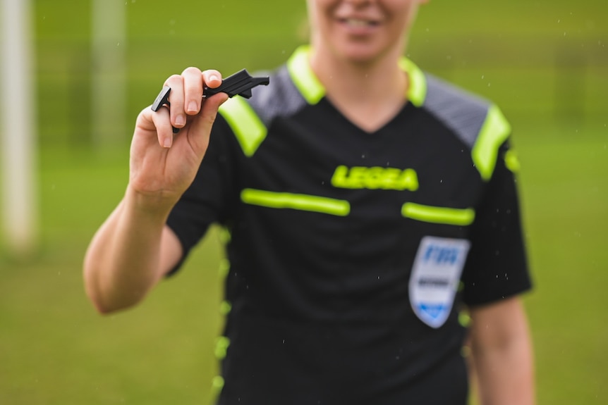 Close up photo of A-League referee Casey Reibelt holding her whistle to the camera