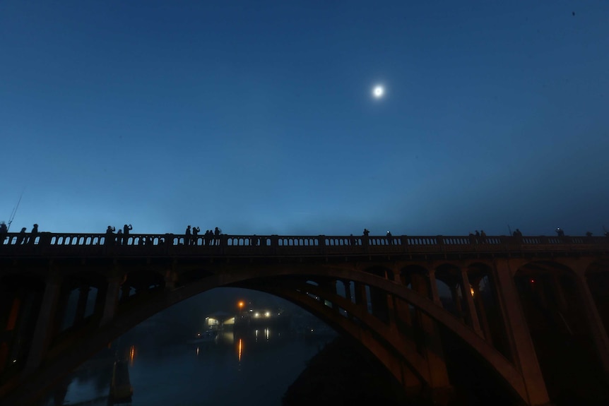 People gather on a bridge and take photos as the total solar eclipse occurs in Oregon, creating an eerie light.